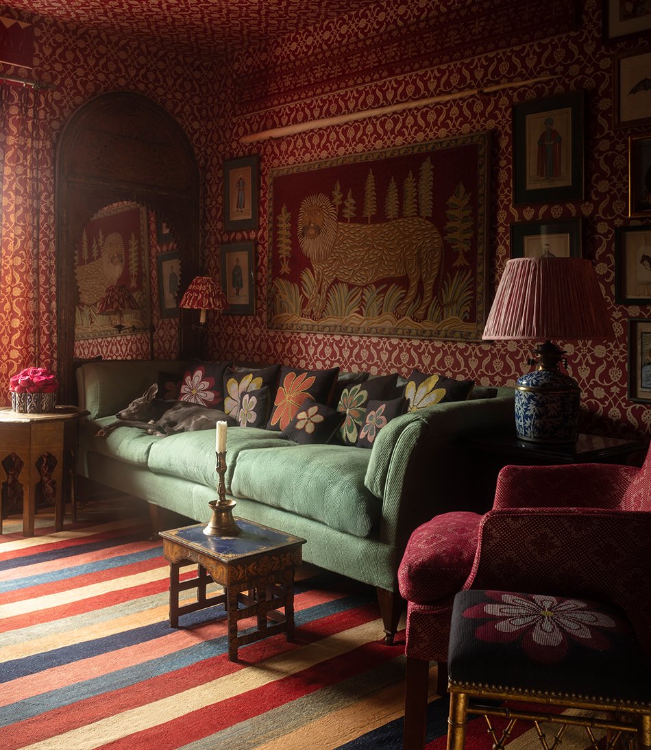 Green sofa with floral cushions, dog lying in corner. Red and white floral wallpaper across all walls