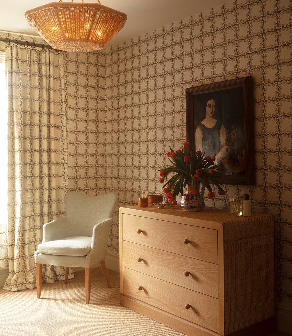 Espalier Square Chestnut fabric as curtains behind a blue armchair and rattan chest of drawers 