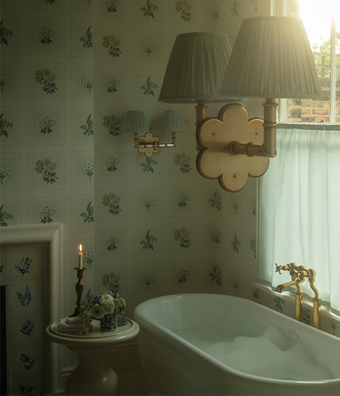 Etoile Blue fabric in a bathroom with a blue and white wallpaper and tiled fireplace and a white bathtub, table and candle