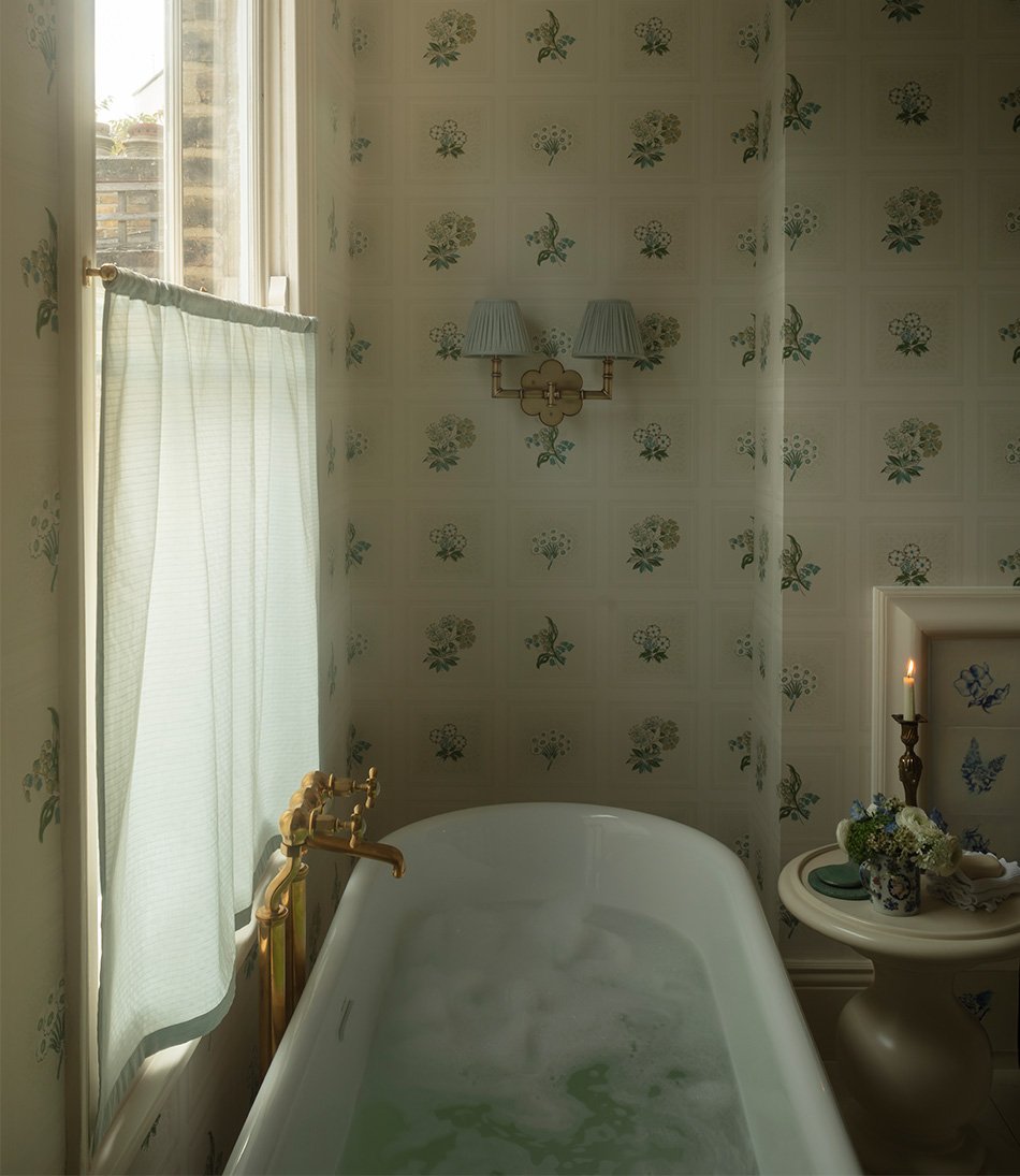 Etoile Blue fabric in a bathroom with a blue and white wallpaper and tiled fireplace and a white bathtub, table and candle