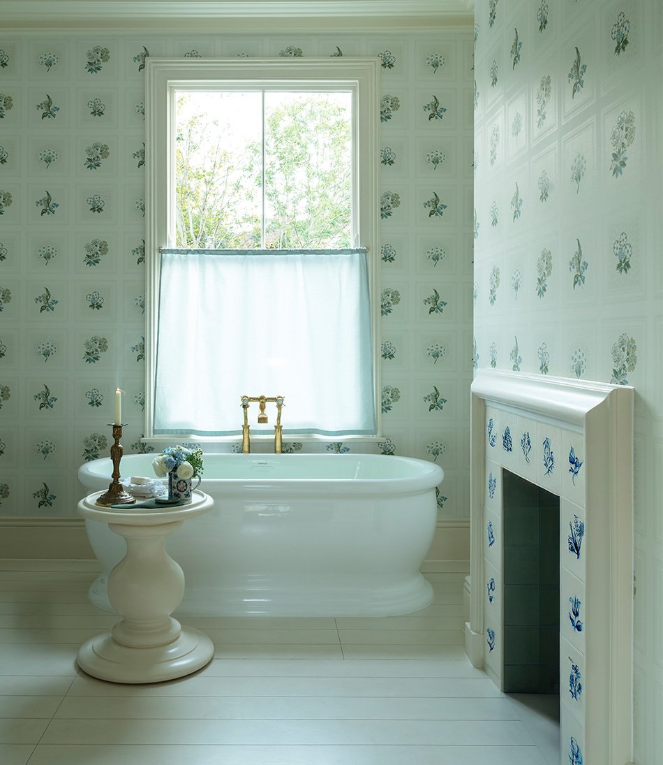 Etoile Blue fabric in a bathroom with a blue and white wallpaper and tiled fireplace and a white bathtub, table and candle