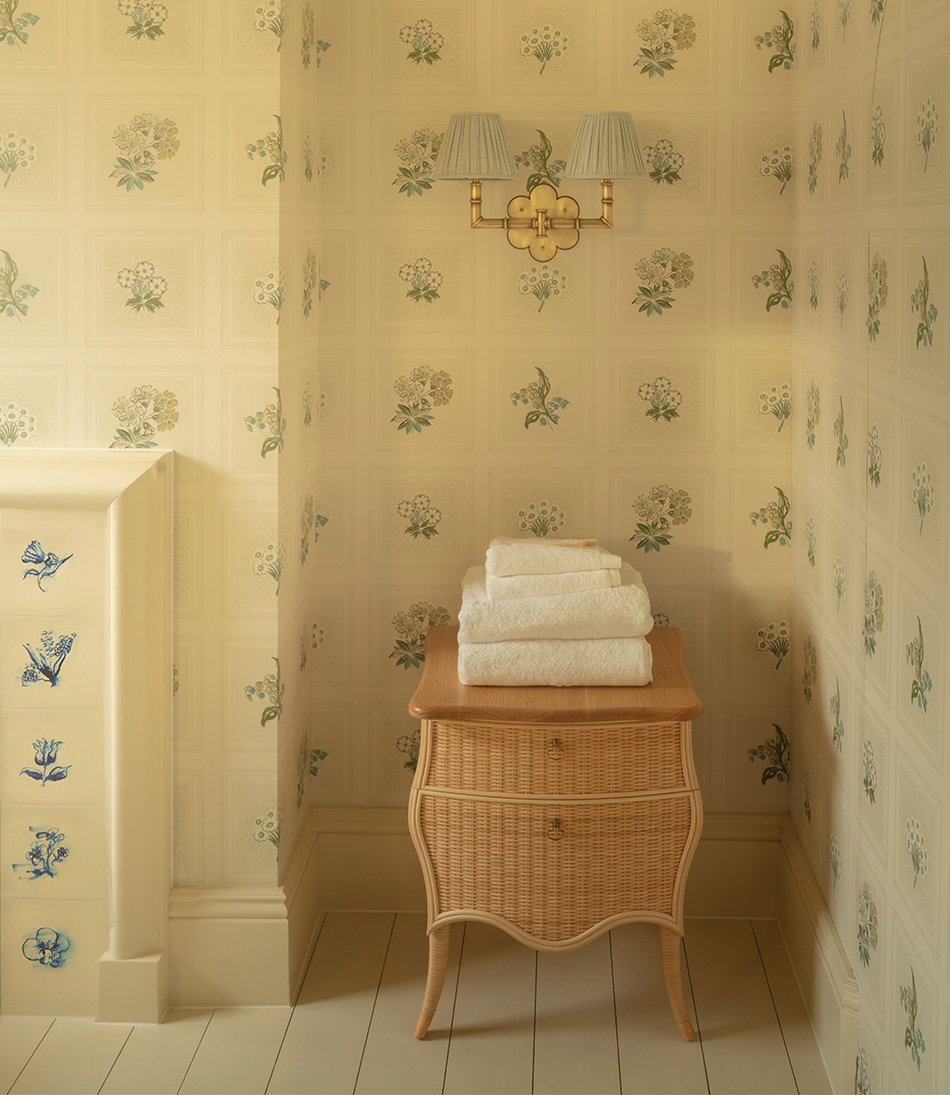 Linnaeus Original Wallpaper in bathroom with small rattan chest and brass wall lights