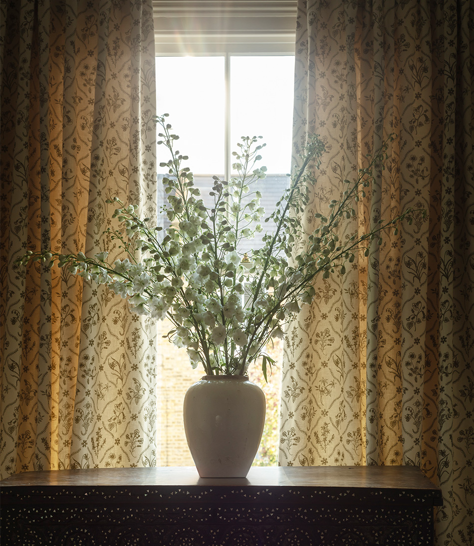 Lucknawi Flower Moss long curtains behind an antique chest with a large vase of flowers