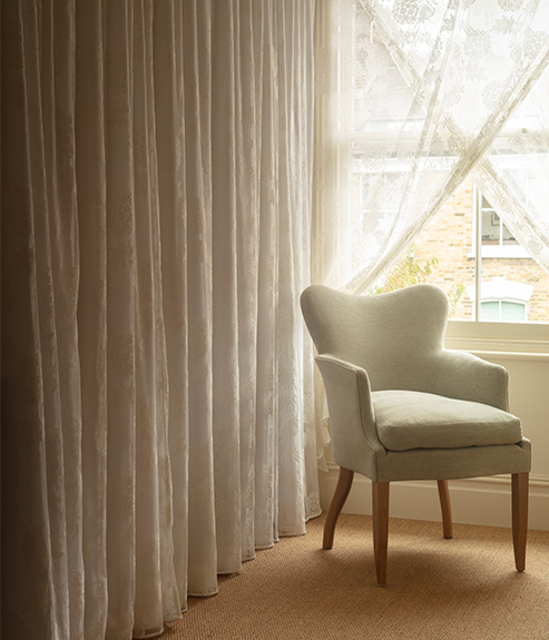 Mole Celadon upholstered armchair in front of a lace curtain