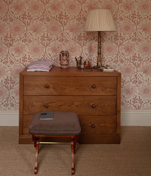 Palampore Blossom Indian Pink wallpaper in a bedroom with a chest and stool 
