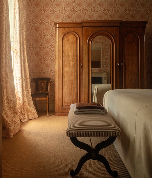 Palampore Blossom Indian Pink wallpaper in a bedroom with a bench and cupboard