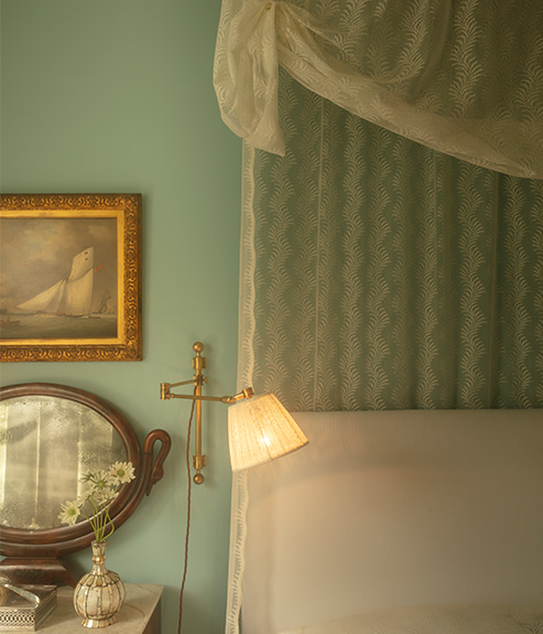 Scrolling Fern Silhouette Lace as a bed curtain and bed cover with wooden bedside tables and brass wall lights