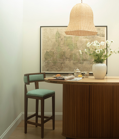 The Rattan Big Bad Kitty hanging light above a bar with a vase of large white flowers and a green counter height stool