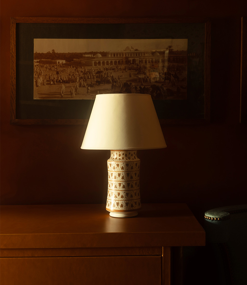 The Apothecary Lamp Vitis is a small gold and ivory timber lamp on a orange leather cabinet and a blue chair 