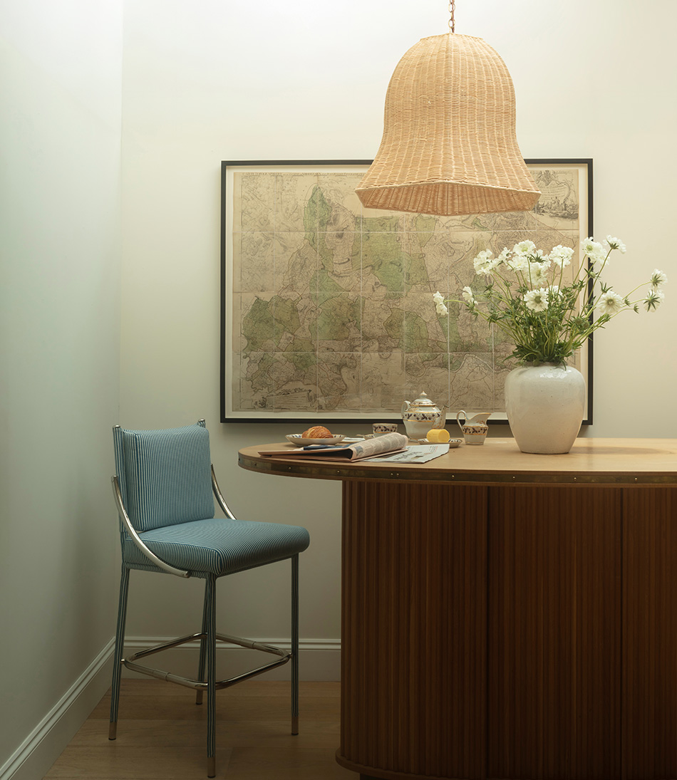 The Rattan Big Bad Kitty hanging light above a bar with a vase of large white flowers and a blue and white counter height stool