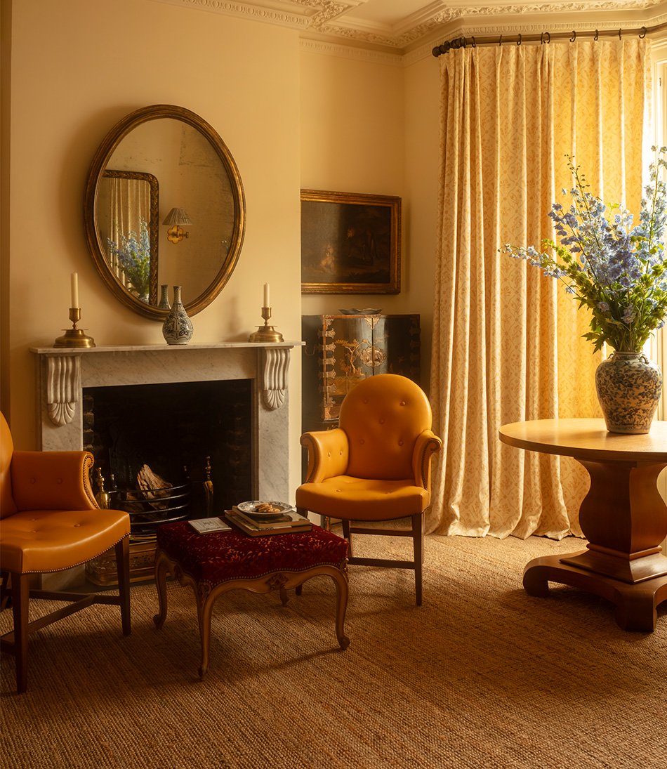 The Moonback chair in a yellow leather in front of a fireplace and long yellow curtains