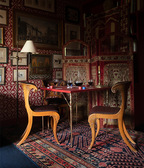 The Pierre Card Table set with a poker game and two antique wooden chairs