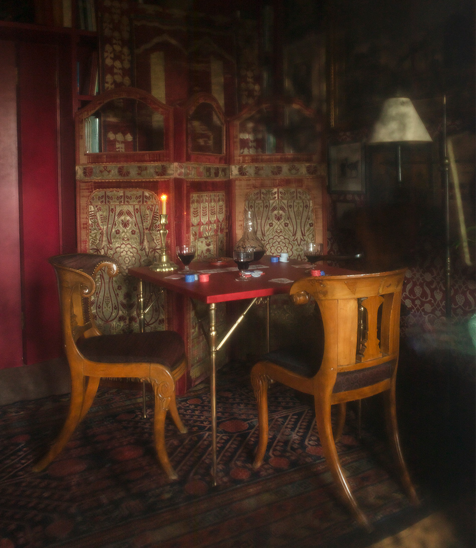 The Pierre Card Table set with a poker game and two antique wooden chairs