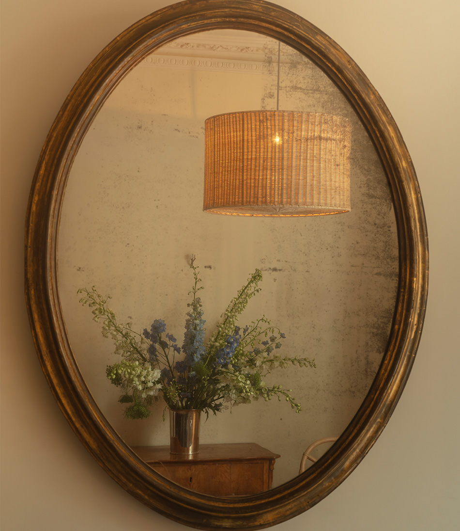 The Rattan Drum Hanging Light with Diffuser in a reflection of an antique gold mirror 