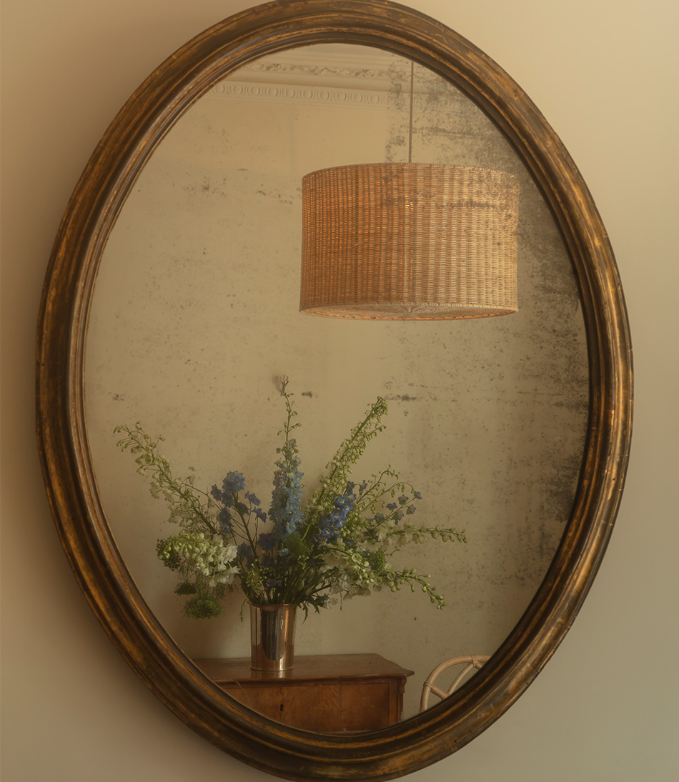 The Rattan Drum Hanging Light with Diffuser in a reflection of an antique gold mirror 
