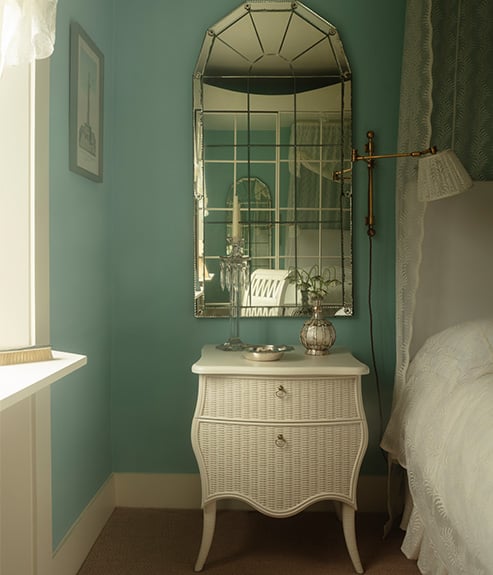 The Virginia Chest in a blue bedroom with a glass segmented mirror and lace curtains 