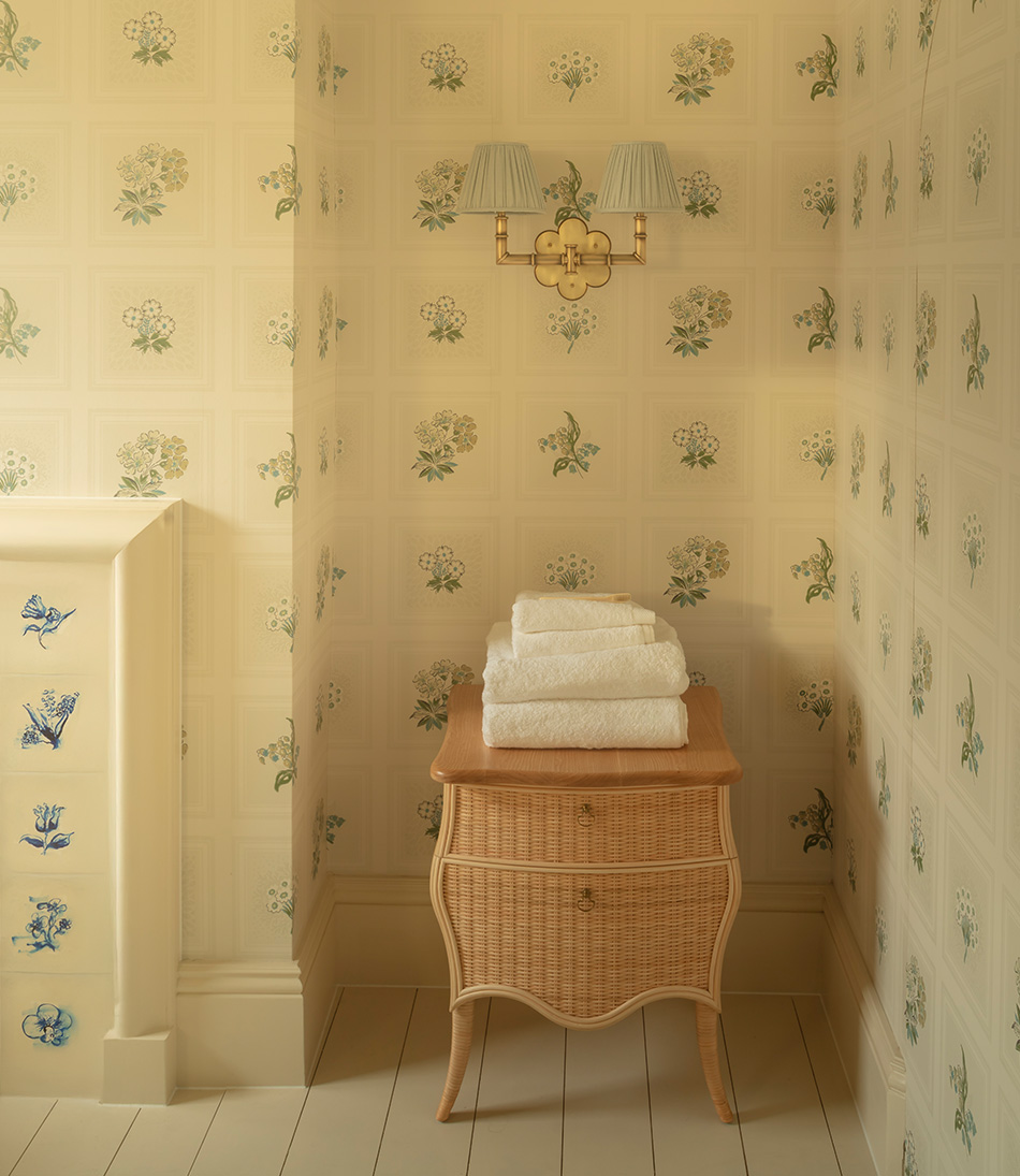 The Virginia Chest in natural rattan, in a blue and white bathroom with a brass double wall light with blue shades 